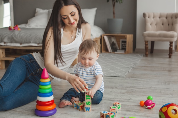 Junge hübsche Mutter spielt mit ihrem kleinen Sohn. Fröhliche Familie, die Spaß drinnen mit kleinem kleinen Sohn hat