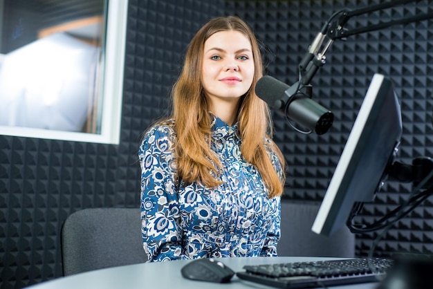 Junge hübsche Radiomoderatorin, die mit Kopfhörern im Studio sitzt und in der Luft spricht