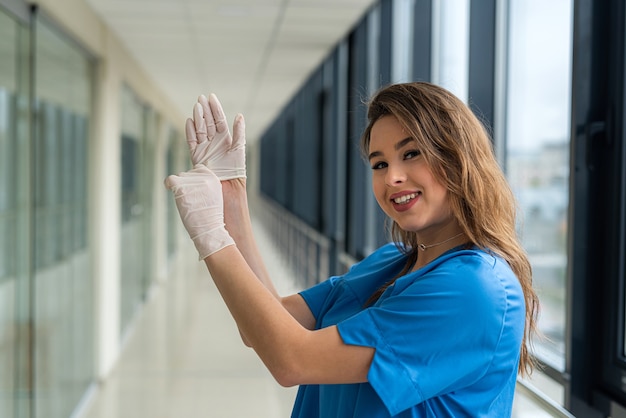 Junge hübsche Ärztin in blauer Uniform mit schützenden weißen Handschuhen, um die Ausbreitung des Coronavirus zu verhindern