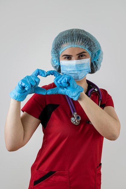 Junge hübsche Ärztin in roter Uniform zeigt Herz-Symbol-Form mit Händen auf Weiß
