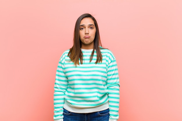 Junge hübsche spanische Frau, die traurig und gestresst ist, verärgert wegen einer schlechten Überraschung, mit einem negativen, ängstlichen Blick gegen rosa Wand