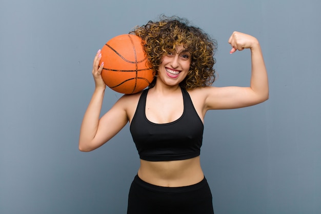 Junge hübsche Sportfrau, die Fitnesskleidung mit einem Basketball trägt