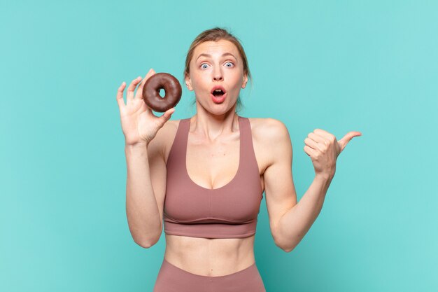 Junge hübsche Sportfrau erschrocken Ausdruck und hält einen Donut