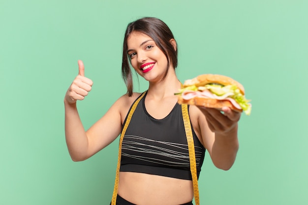 Junge hübsche Sportfrau glücklicher Ausdruck und hält ein Sandwich