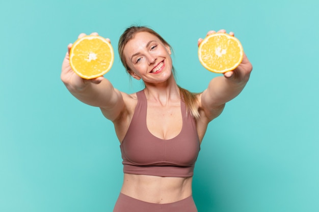 Junge hübsche Sportfrau glücklicher Ausdruck und hält eine Orange