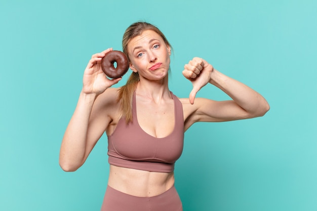 Junge hübsche Sportfrau trauriger Ausdruck und hält einen Donut