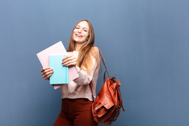 Junge hübsche studentenfrau mit blauer wand der bücher und der tasche mit einem kopienraum