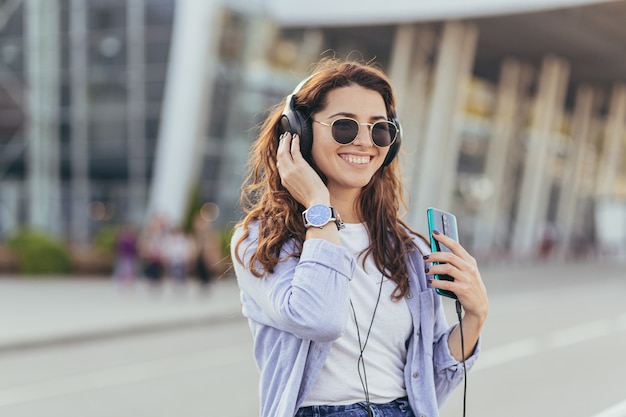 Junge hübsche Studentin, die auf ein Taxi wartet und Musik hört