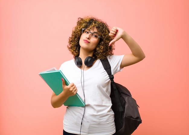 Junge hübsche Studentin, die stolz, arrogant und selbstbewusst fühlt, zufrieden und erfolgreich aussieht und auf sich selbst gegen rosa Wand zeigt