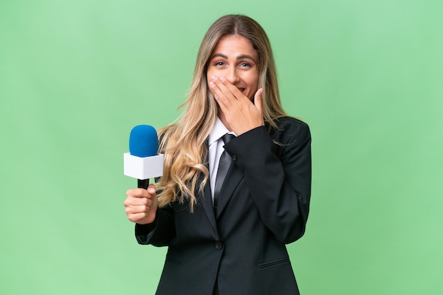 Junge hübsche uruguayische Fernsehmoderatorin vor isoliertem Hintergrund, glücklich und lächelnd, den Mund mit der Hand bedeckend