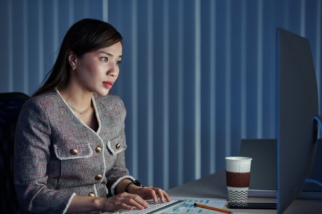 Junge hübsche vietnamesische Geschäftsfrau, die trinkt, nimmt Kaffee weg, wenn sie den ganzen Tag im Büro arbeitet und großes Projekt innerhalb der Frist beendet