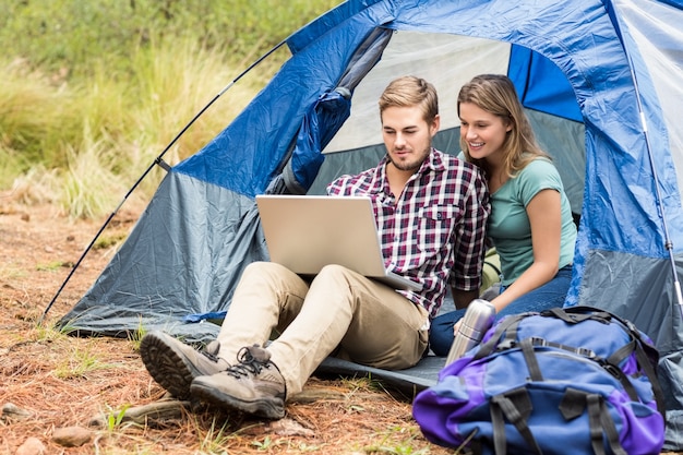 Junge hübsche Wandererpaare, die in einem Zelt betrachtet Laptop sitzen