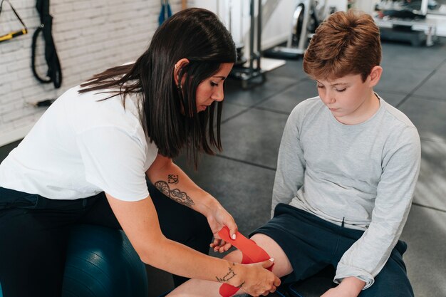 Junge im Alter von 10 Jahren mit einer Beinverletzung und wird von einem Physiotherapeuten unterstützt, während er ihn festhält, damit er sich schneller erholen kann