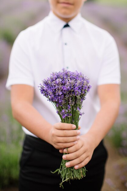 Junge im eleganten Anzug mit Lavendelblumenstrauß, der auf dem Veilchenfeld der Provence in die Kamera blickt.