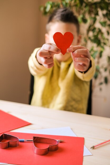 Foto junge im gelben t-shirt zeigt ein handgemachtes rotes papierherz