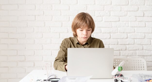 Junge im grünen Hemd, das zu Hause am Laptop arbeitet oder studiert