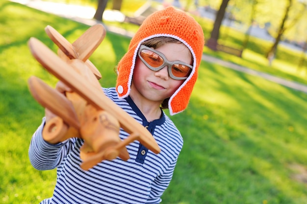 Foto junge im orange sturzhelmpilot, der in der hölzernen fläche des spielzeugs gegen gras spielt