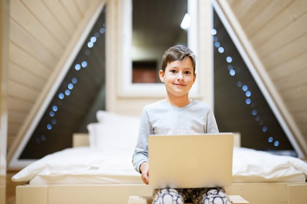 Junge im Pyjama sitzen mit Laptop in der Holzhütte zu Hause Konzept des Glücks der Freizeitbeschäftigung in der Kindheit