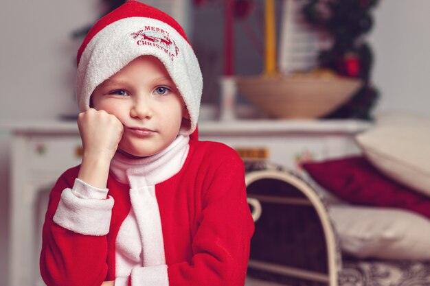 Junge im roten Anzug wie der Weihnachtsmann in einem schönen Raum gekleidet