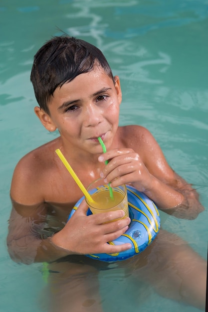 Junge im Wasser trinkt ein Getränk aus einem Strohhalm und lächelt Sommerferien