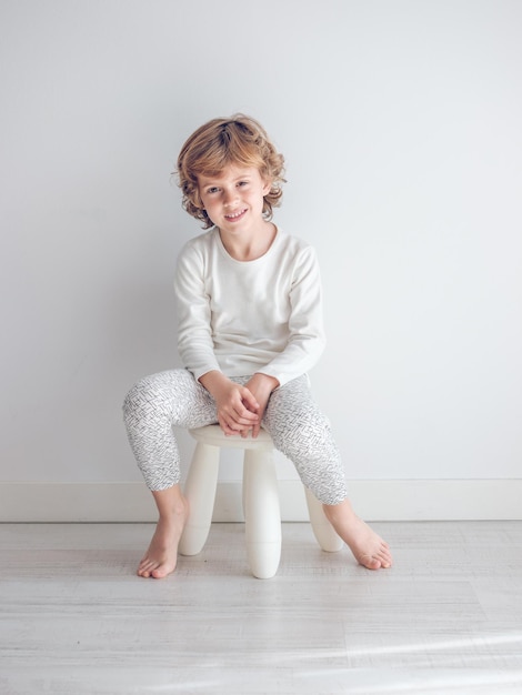 Junge im weißen Pyjama lehnt an der weißen Wand seines Hauses.