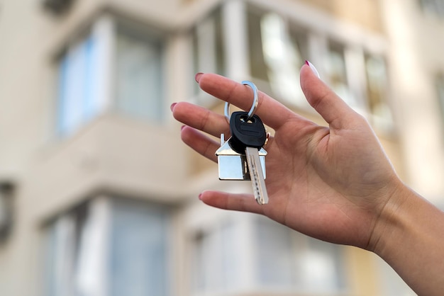 Junge Immobilienmaklerin lächelt selbstbewusst und hält den Schlüssel zum neuen Haus in der Nähe des neuen Hauses das Konzept, ein Haus zu verkaufen