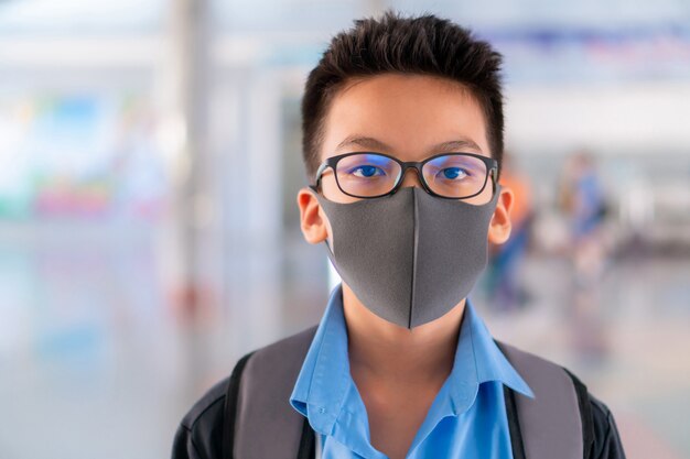 Junge in der Schuluniform, die eine chirurgische Maske mit unscharfem Hintergrund trägt, Virusschutzkonzept.