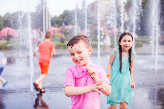 Junge in einem nassen rosafarbenen T-Shirt steht mit seinen Freunden um einen Jet-Brunnen herum, in dem Wasser spritzt