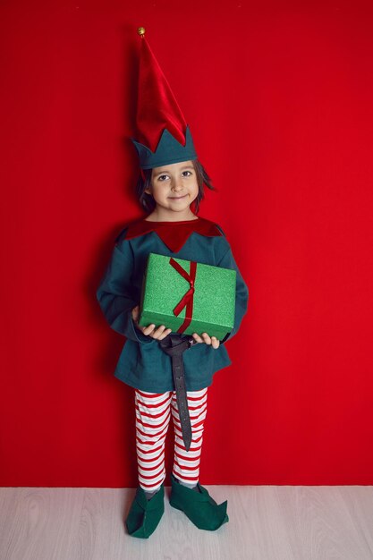 Junge in einem Zwergenkostüm steht am Weihnachtstag auf rotem Grund