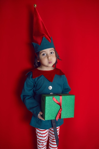 Junge in einem Zwergenkostüm steht am Weihnachtstag auf rotem Grund