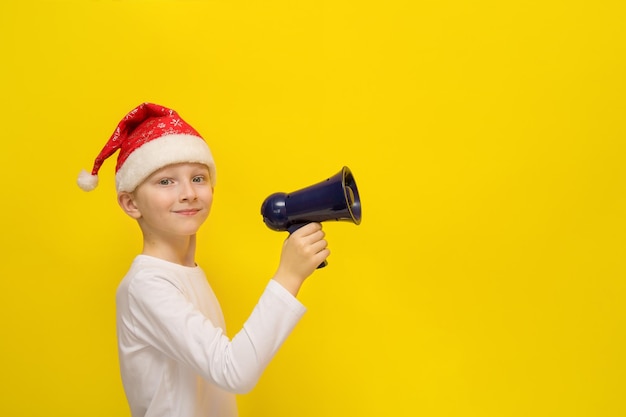 Junge in einer Weihnachtsmütze hält ein Megaphon in seinen Händen auf gelbem Hintergrund mit Kopierraum Weihnachtswinterferien