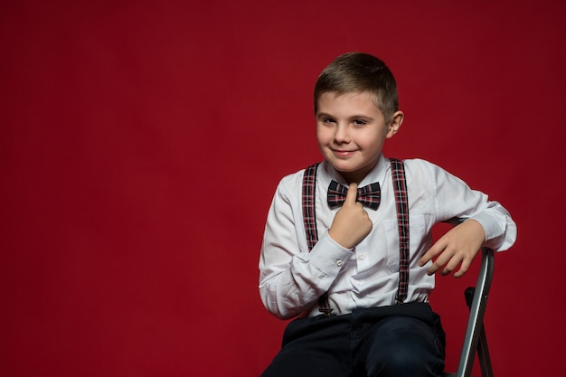 Junge in eleganten Kleidern sitzt auf einer eisernen Trittleiter gegen rote Wand