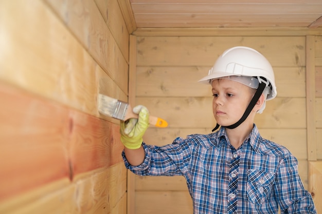 Junge in Schutzfarbe malt die Wand eines Holzhauses, das auf einer Leiter steht. ein Holzhaus von innen mit Öl für Holz streichen