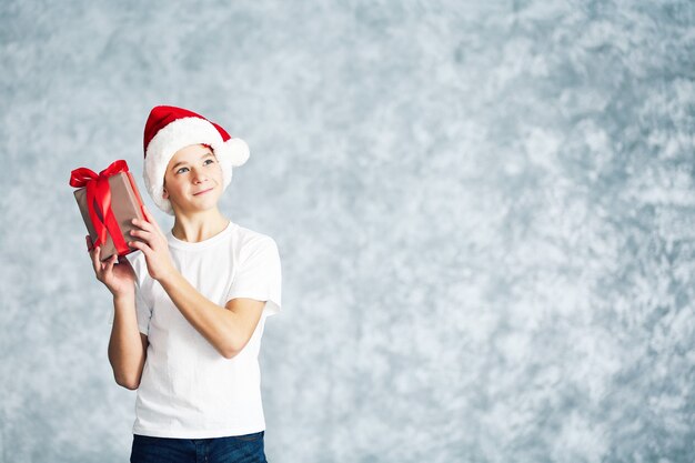 Junge in Weihnachtsmütze mit Geschenkbox auf grauem Hintergrund