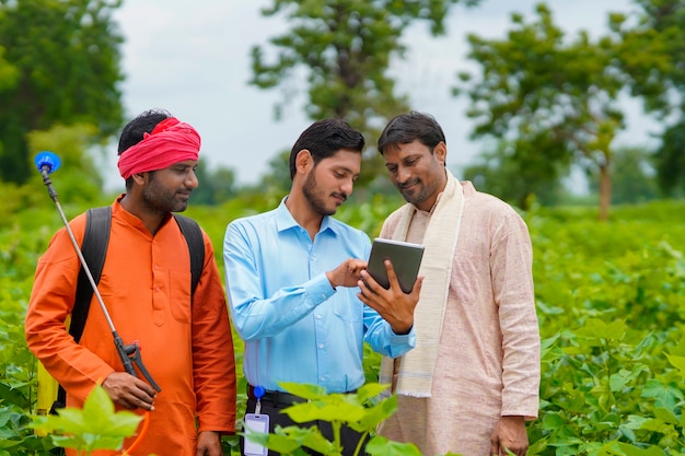 Junge indische Agronomen oder Banker, die dem Landwirt in Tablette auf dem Landwirtschaftsfeld einige Informationen zeigen.