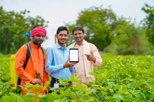 Junge indische Agronomen oder Banker, die Smartphone mit Landwirten auf dem Landwirtschaftsfeld zeigen.