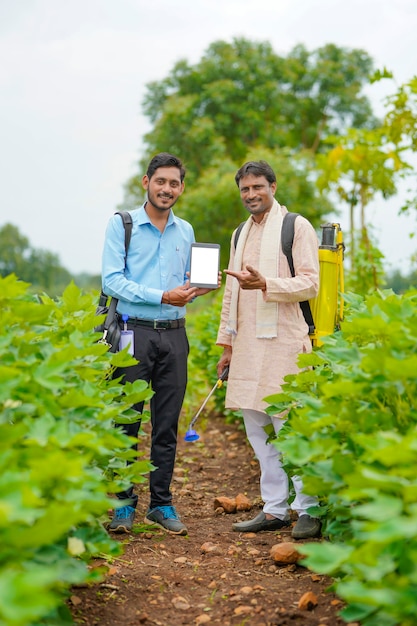 Junge indische Agronomen oder Banker, die Tablette mit Landwirt am Landwirtschaftsfeld zeigen.