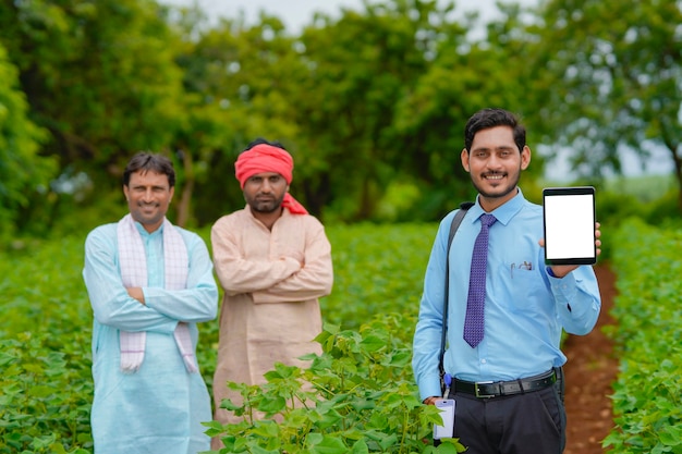 Junge indische agronomen oder banker, die tablette mit landwirten auf dem landwirtschaftsfeld zeigen.