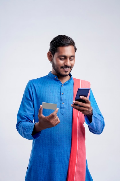 Junge indische Bauer mit Smartphone und Bankkarte auf weißem Hintergrund.
