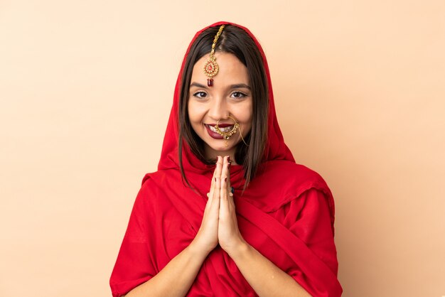 Junge indische Frau auf beige Wand hält Handfläche zusammen