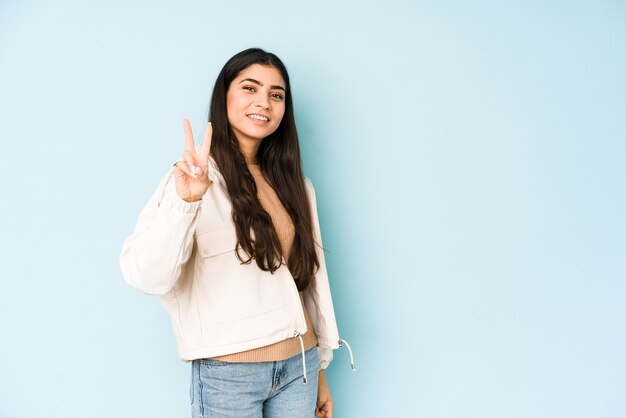 Junge indische Frau auf blauer Wand, die Nummer zwei mit den Fingern zeigt.