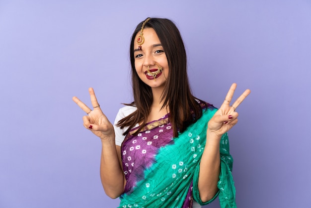 Junge indische Frau auf lila Wand, die Siegeszeichen mit beiden Händen zeigt