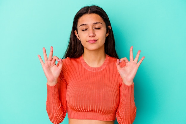 Junge indische Frau, die auf Blau isoliert ist, entspannt sich nach hartem Arbeitstag, sie führt Yoga durch.