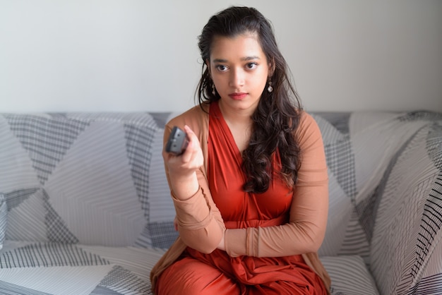 Junge indische Frau, die ernst schaut, während sie im Wohnzimmer zu Hause fernsieht