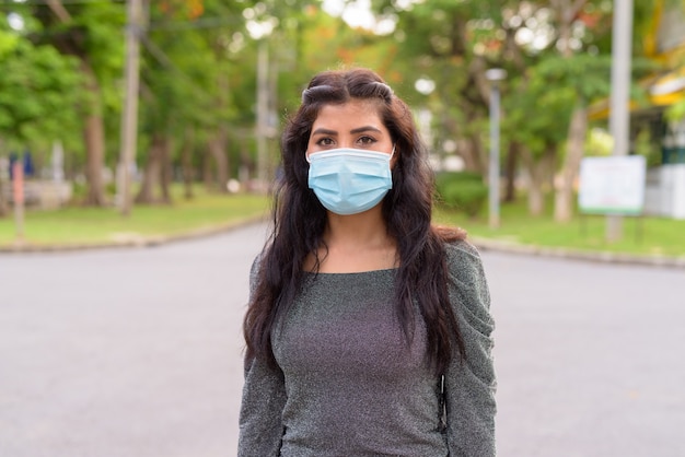 Junge indische Frau, die Maske zum Schutz vor Coronavirus-Ausbruch am Park im Freien trägt