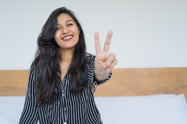 Junge indische Frau, die Sieggeste im Schlafzimmer tut