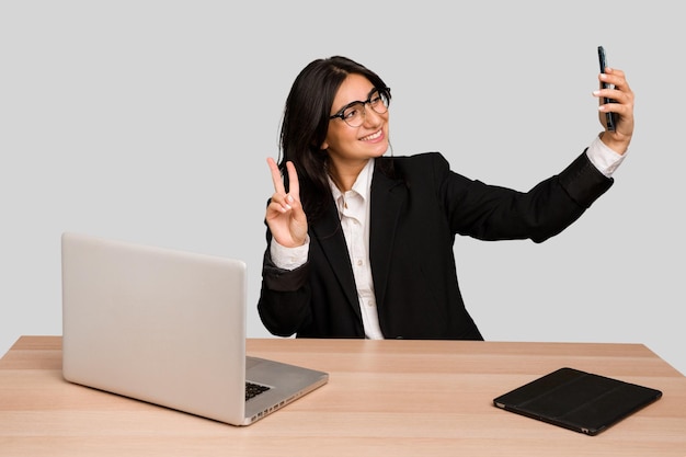 Junge indische frau in einem tisch mit einem laptop und einem tablet unter verwendung eines handys isoliert