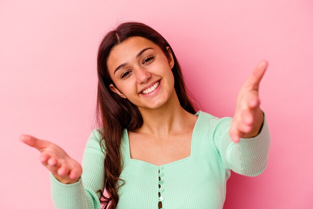 Junge indische Frau isoliert auf Rosa, die einen willkommenen Ausdruck zeigt.