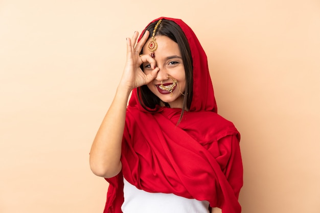 Junge indische Frau lokalisiert auf beige Wand, die ok Zeichen mit Fingern zeigt