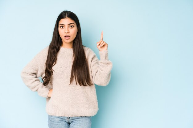 Junge indische Frau lokalisiert auf blauer Wand, die oben mit geöffnetem Mund zeigt.